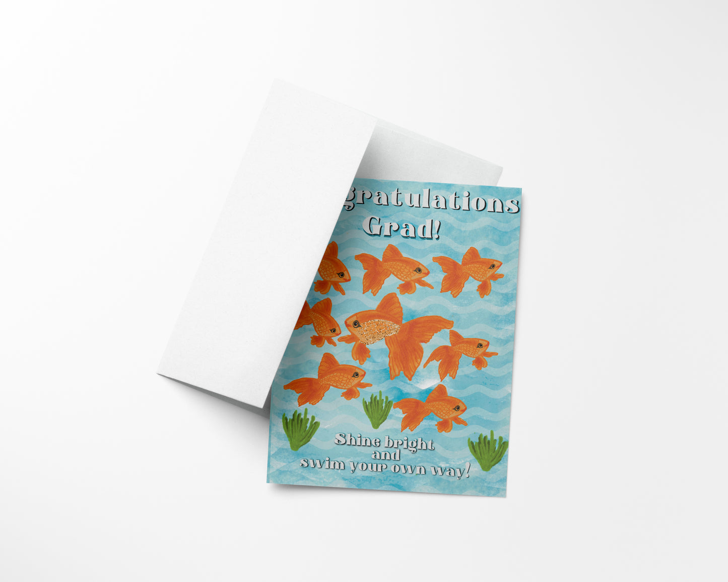 “A white greeting card envelope partially revealing a blue card with nine goldfish, seaweed, and the text “Congratulations Grad! Shine bright and swim your own way!”"