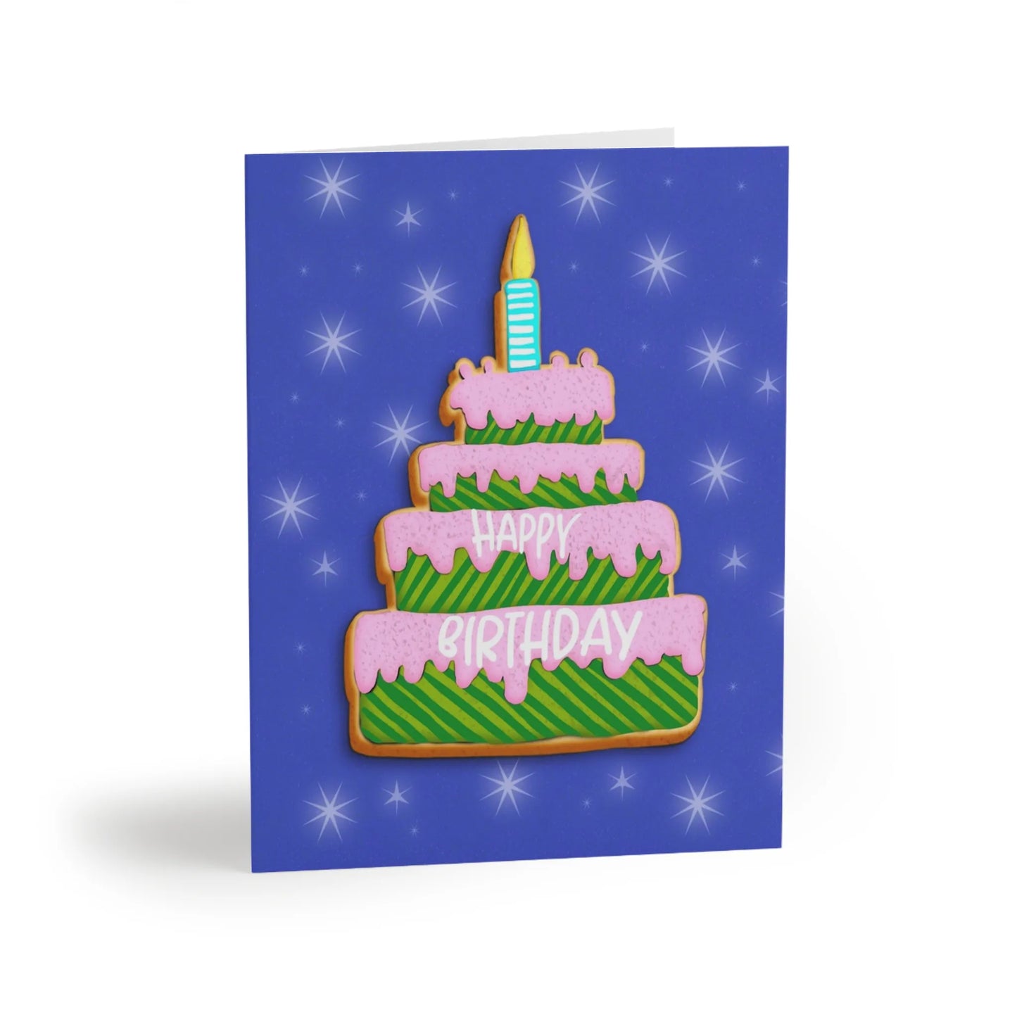 “A birthday card with a tiered cookie cake design, pink frosting, green striped cake, and cookie trim, on a blue star-filled background. The words "HAPPY BIRTHDAY" are on the cake.”