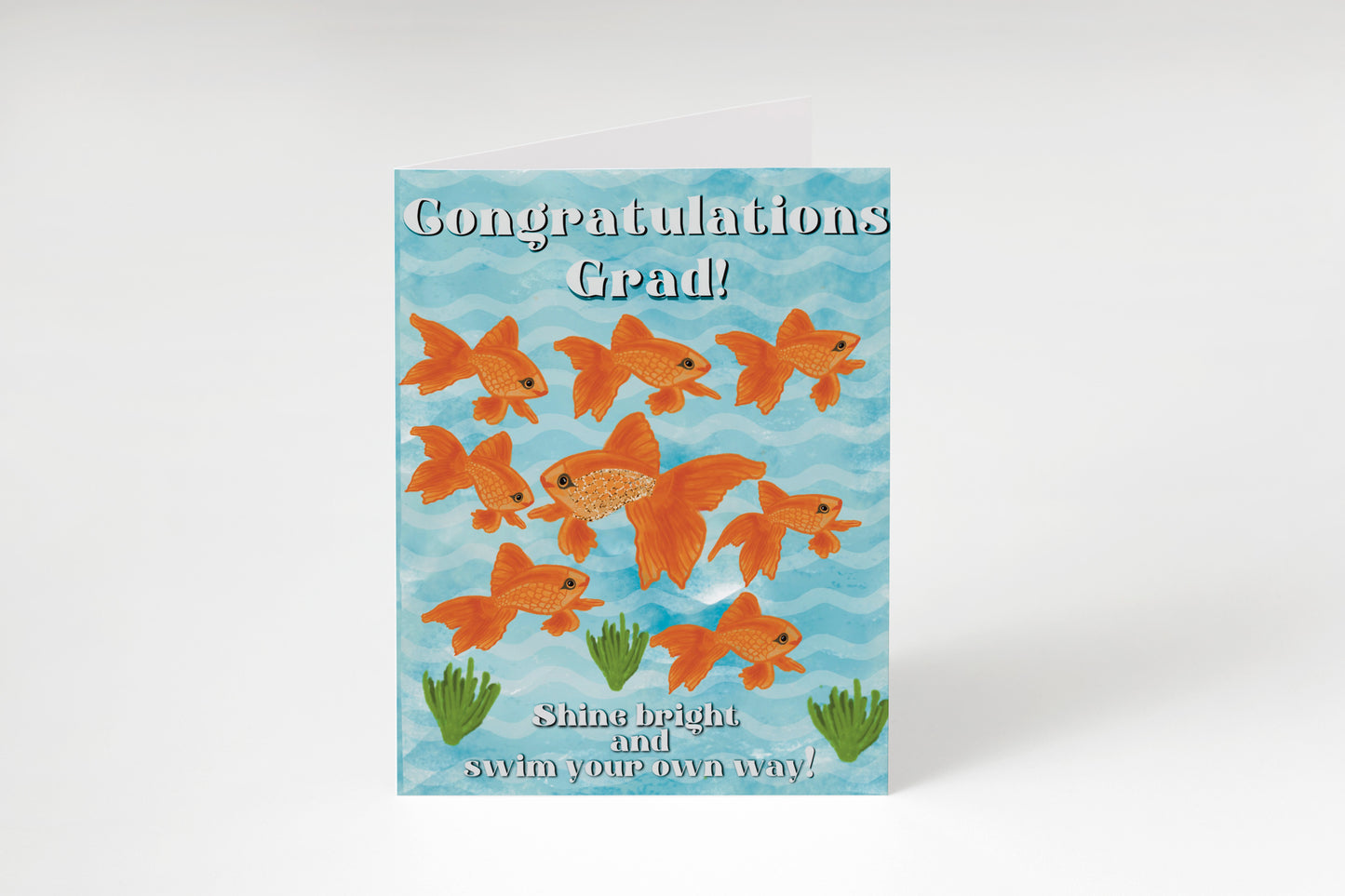 “Graduation card with a light blue wavy background, nine orange goldfish, and green seaweed. Text: "Congratulations Grad! Shine bright and swim your own way!”"