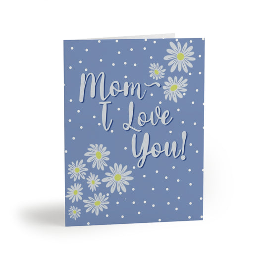 “A light blue card with white polka dots, white daisies with yellow centers, and the text "Mom I Love You!" in white script.”