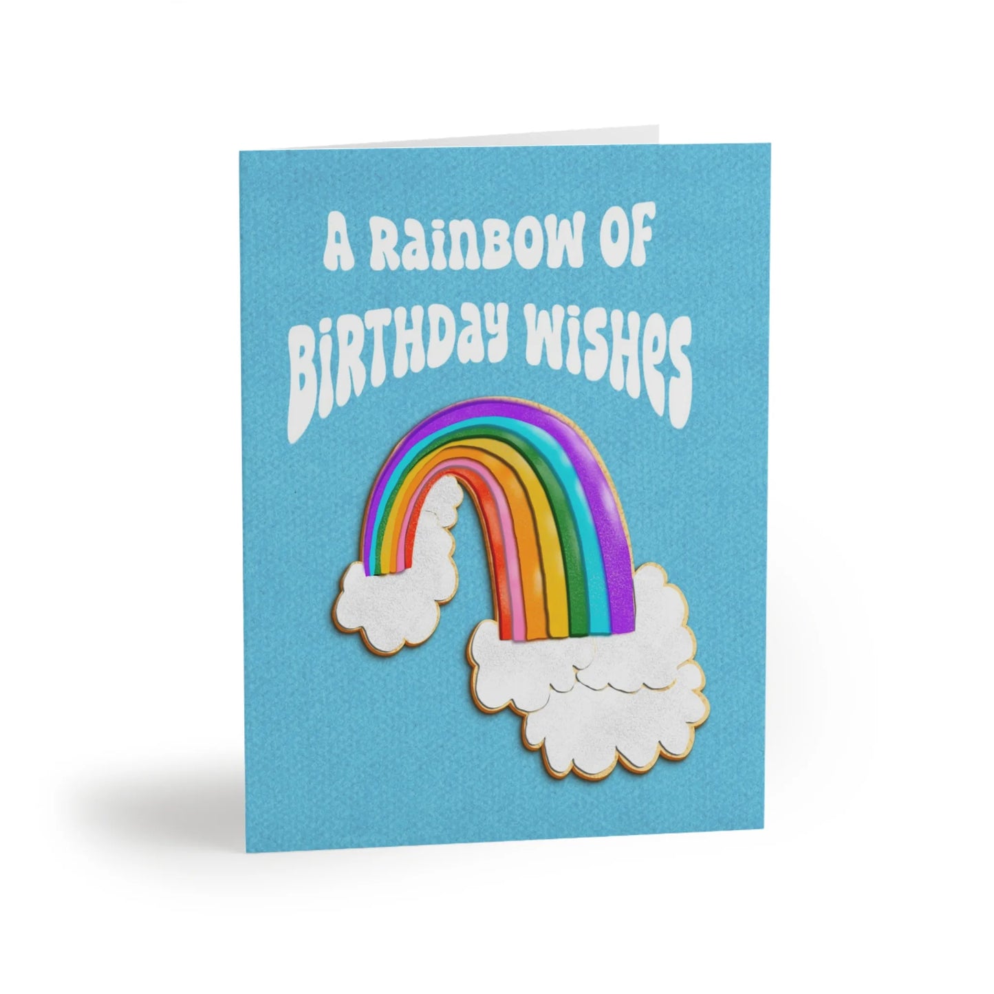 Light blue birthday card with a cookie cake of a bright rainbow and two clouds; text reads "A Rainbow of Birthday Wishes".