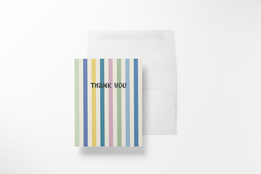 A vertical striped thank you card with pastel vertical stripes in green, yellow, pink, blue, and white, with the words 'THANK YOU' printed in black. A plain white envelope is placed behind it on a clean white background.