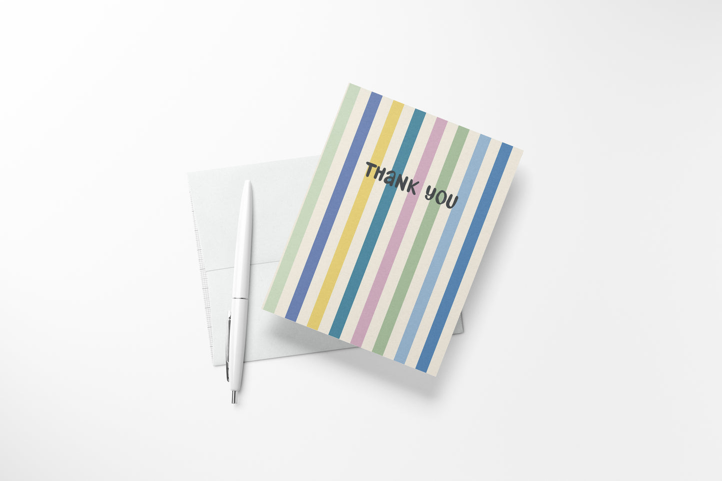 An A2  thank-you card with vertical pastel stripes in blue, green, yellow, pink, and purple, placed on top of a white envelope with a white pen beside it on a light background.