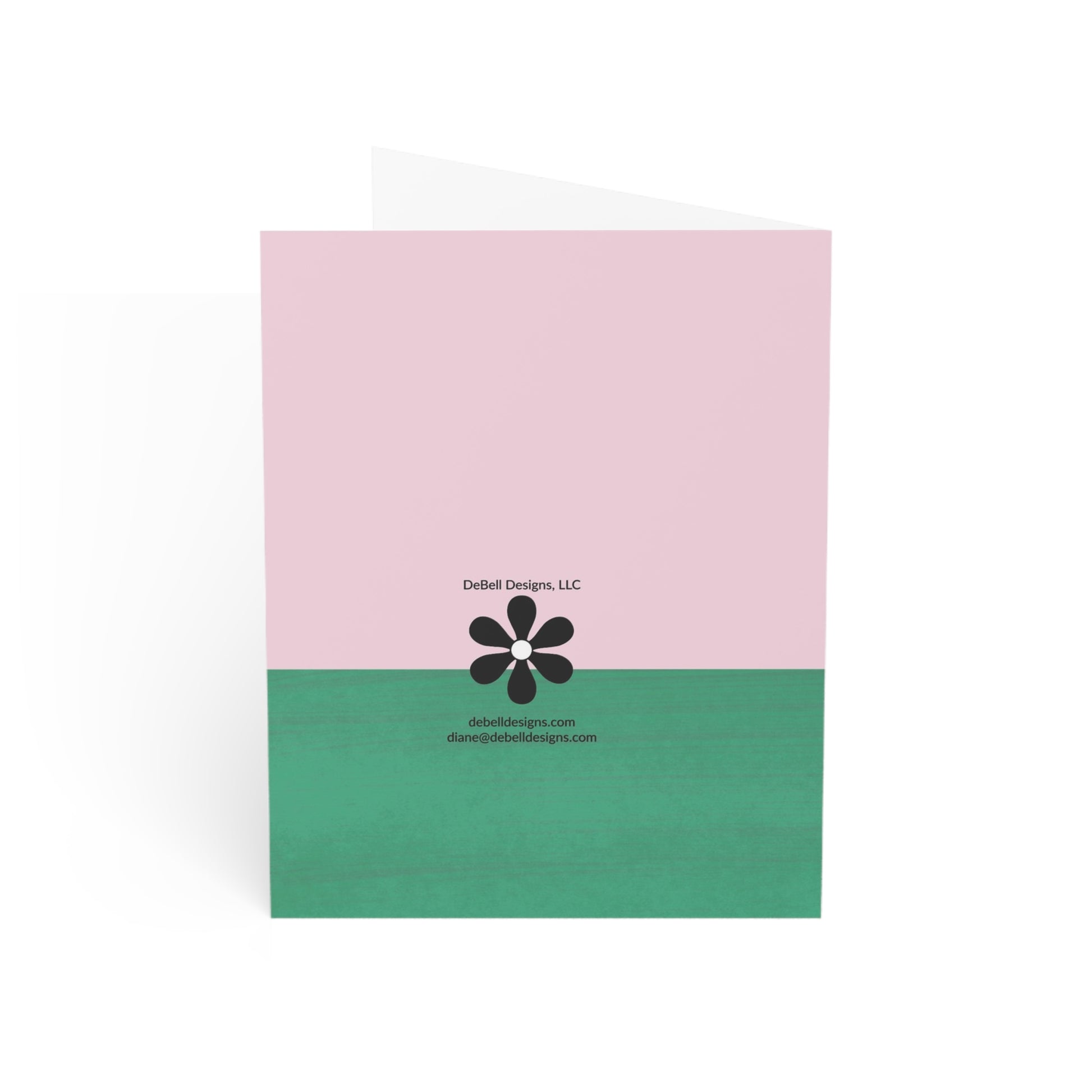 A vertically-oriented folded card, solid pink upper half, and green lower half. A black flower with a white center and the text "DeBell Designs, LLC debelldesigns.com diane@debelldesigns.com" is centered in the card's middle.