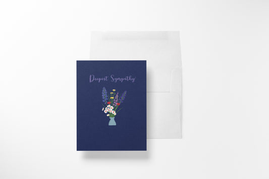 A navy blue greeting card with 'Deepest Sympathy' and a small floral hand-illustrated bouquet , shown in front of a white envelope.
