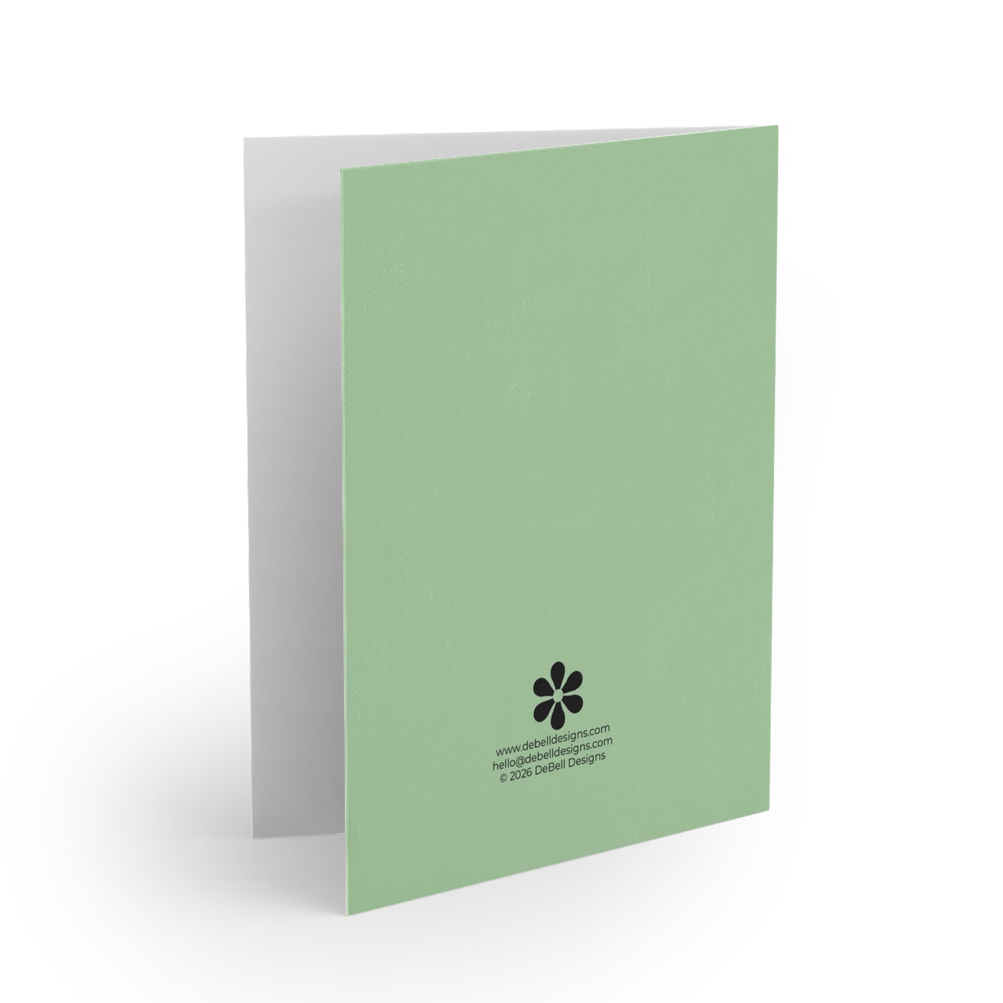 A light green folded greeting card stands vertically, angled right, with a gray interior and fine texture. Black text and a flower logo are at the bottom right.