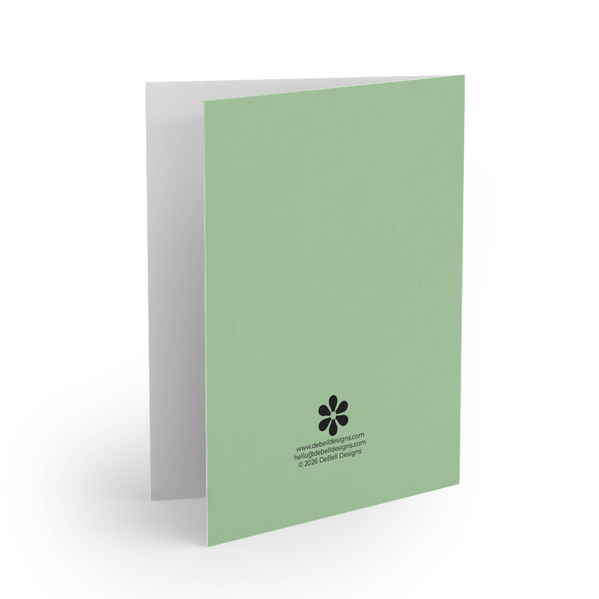 A light green folded greeting card stands vertically, angled right, with a gray interior and fine texture. Black text and a flower logo are at the bottom right.