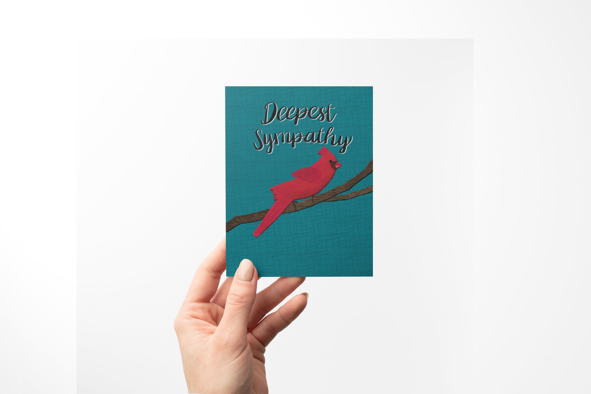 A hand holding a teal sympathy card featuring a red cardinal on a branch with the text 'Deepest Sympathy' in black script, shadowed in white set against a plain white background.
