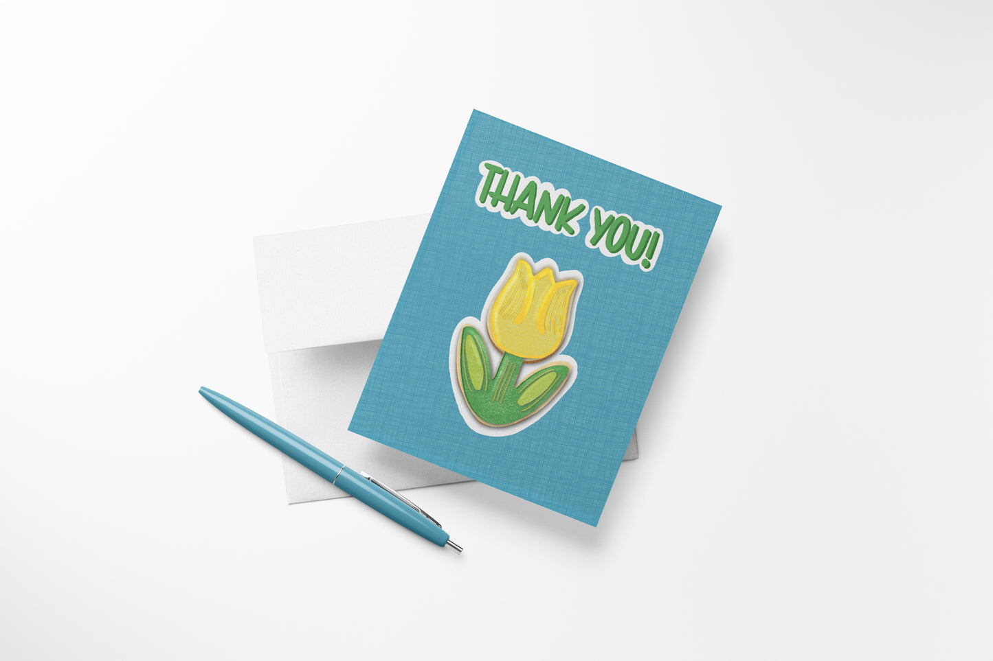 Hand-illustrated Thank You Tulip Cookie greeting card with a yellow tulip sugar cookie on teal, shown with envelope and pen, ready to write a heartfelt note.