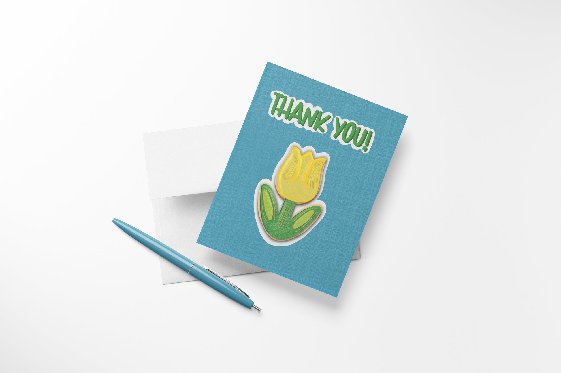 Hand-illustrated Thank You Tulip Cookie greeting card with a yellow tulip sugar cookie on teal, shown with envelope and pen, ready to write a heartfelt note.