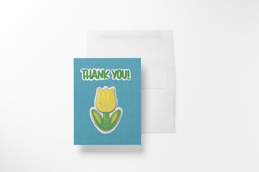 Hand-illustrated Thank You Tulip Cookie greeting card with a yellow tulip sugar cookie on a teal linen background, shown with its white envelope.